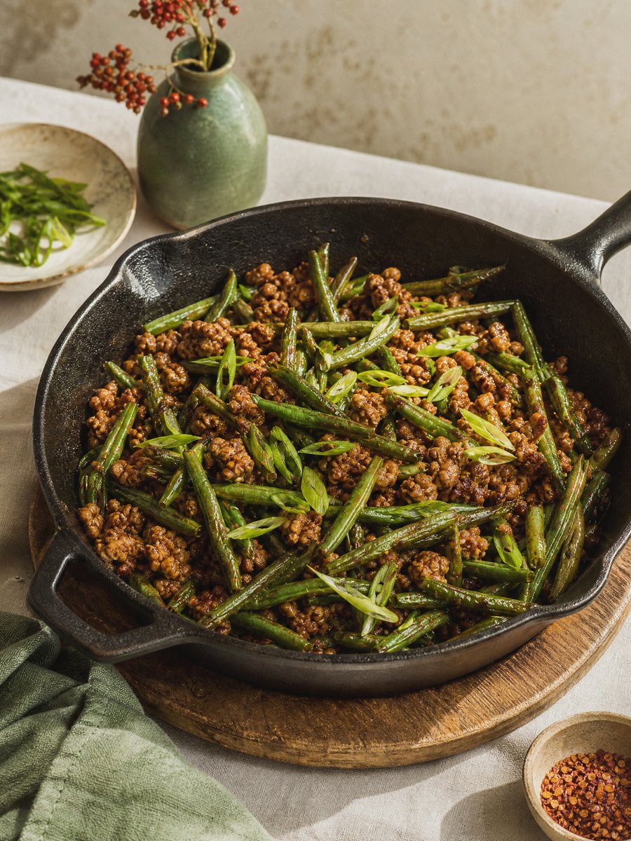 A cast iron skillet filled with browned ground turkey and blistered green beans in a dark soy-ginger sauce, resting on a wooden trivet.